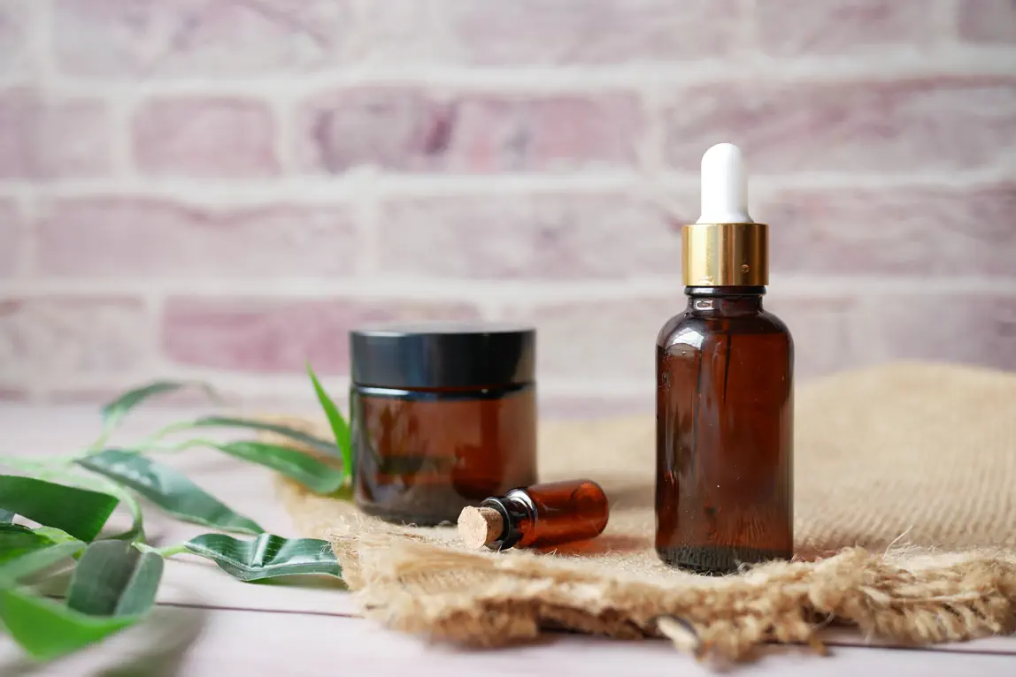 Amber glass bottles with essential oils and natural plant extract products on wooden surface with green leaves