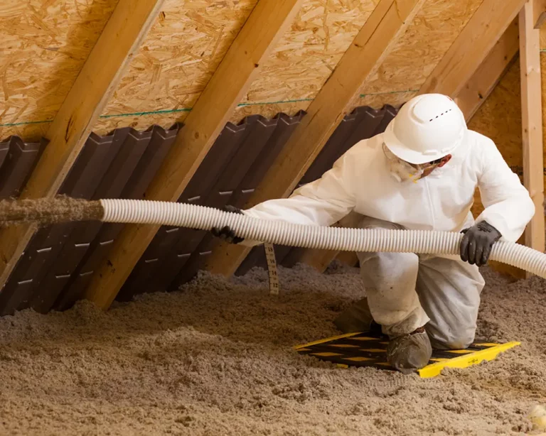Worker in protective suit installing blown insulation in attic rafters for pest prevention