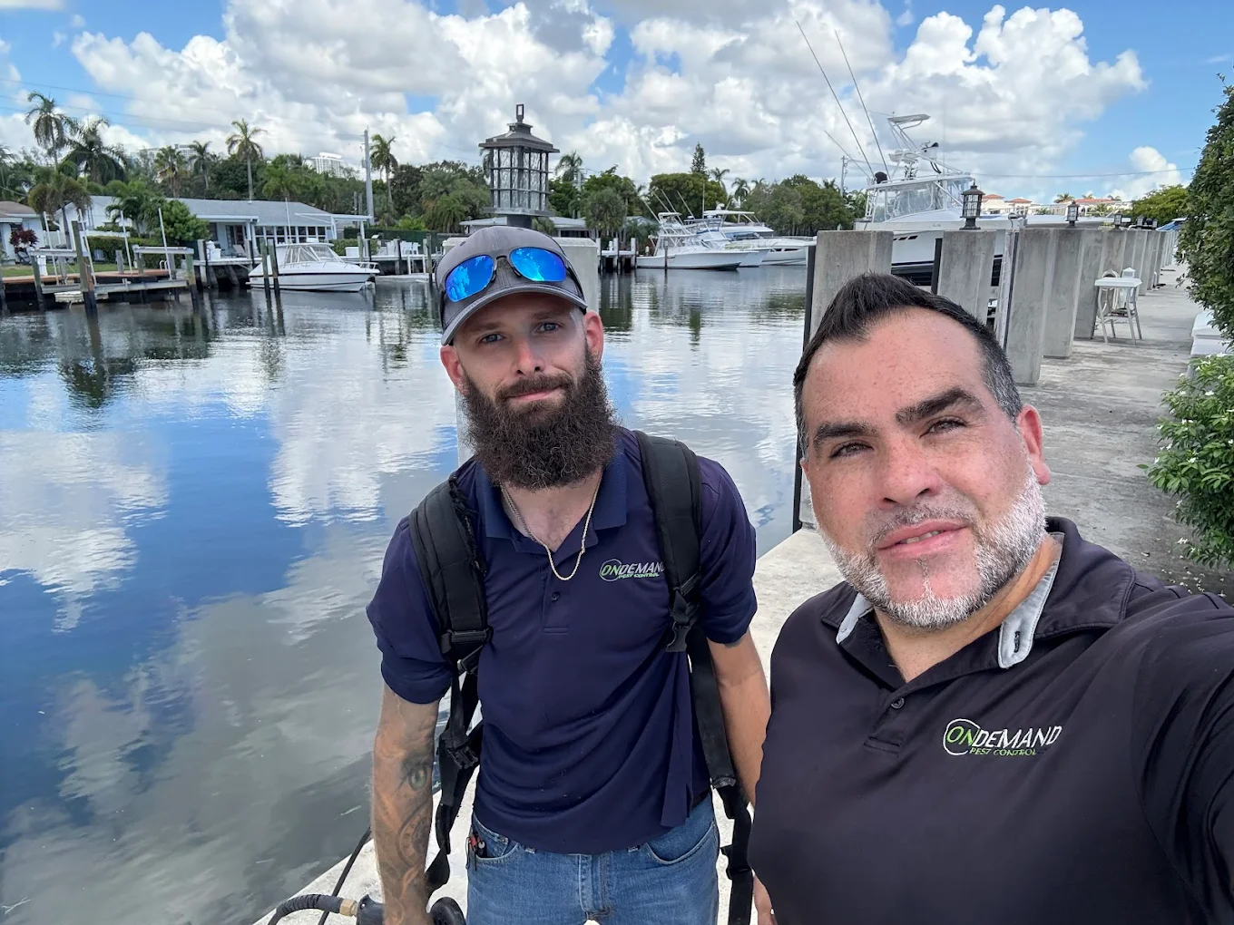Two On Demand Pest Control team members beside a waterfront marina