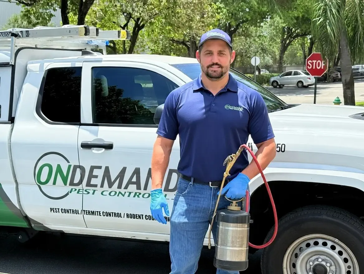 Professional pest control technician in blue uniform with spray equipment standing next to company truck