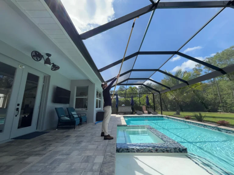 Professional technician cleaning pool enclosure screens with extension pole in residential backyard