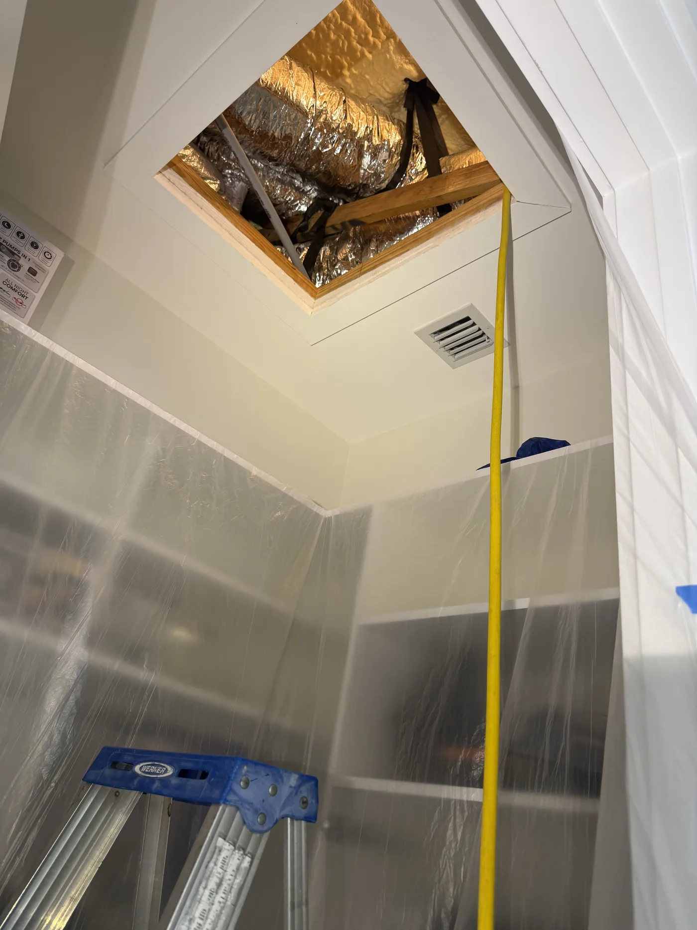 Ceiling attic access showing insulated flexible ducts with plastic sheeting and ladder for inspection