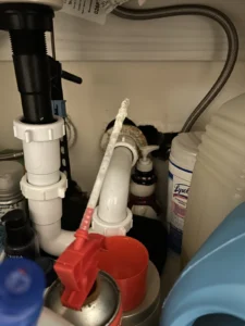 Under-sink plumbing with open, stained pipe penetration through cabinet wall showing possible pest entry point