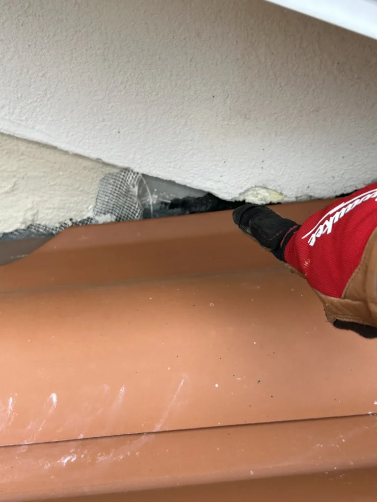Gloved hand inspecting gap with wire mesh between stucco wall and terracotta roof tile